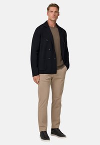 Tumed kahetineuline bleiser pruuni sviitri peal, beežide pükste ja mustade tossudega. Siledad tekstuurid, kohandatud sobivus, meelelahutuslik stiil.