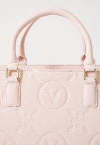 Sac à main texturé rose clair avec des motifs floraux et des cercles en "V" en relief, doté de deux poignées rembourrées fixées par des anneaux en métal doré.