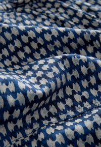 Vævet stof med et blåt og hvidt houndstooth-mønster; glat tekstur med draperede folder, der viser detaljerigdom i designet.