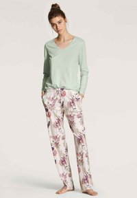 Mintgroene langemouwtop met een V-hals, gecombineerd met pyjamabroek in een bloemenpatroon in het wit, roze en paars. Lichte stof en een relaxte pasvorm.