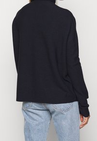 Granatowy sweter z golfem o luźnym kroju, wykonany z miękkiego dzianinowego materiału. Posiada długie rękawy i bezszwowy tył.