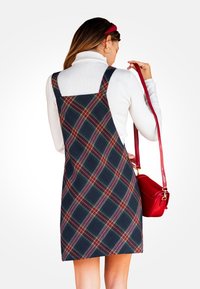 Vestido de tirantes a rayas en azul marino con patrones rojos y verdes. Hecho de tela tejida, presenta tirantes y un corte recto. Sostiene un bolso rojo.