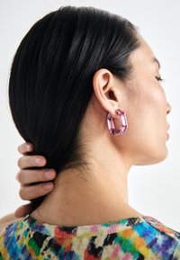 Large pink geometric earrings made of acrylic, featuring an octagonal shape with faceted edges, worn by a person with long dark hair.
