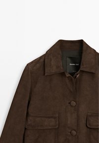 Brown suede jacket featuring a collar, two front pockets, and button closures. The texture is smooth with a matte finish.