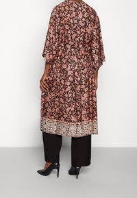 Długi, luźny kimono w ciemno-brązowym materiale z różowym nadrukiem paisley. Ozdobione jasnym, ozdobnym wykończeniem u dołu.