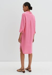 Rosa Leinenkleid mit dreiviertel Ärmeln, Kragen, seitlichen Schlitzen und einem Faltenwurf hinten für zusätzliche Details. Sanfte Textur und lockere Passform.