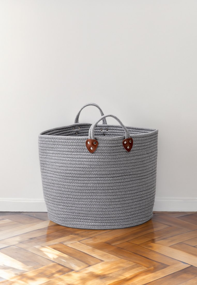 Grauer geflochtener Aufbewahrungskorb mit zwei braunen Ledergriffen und dekorativen Hardware-Akzenten, der eine runde Form und eine strukturierte Oberfläche aufweist.