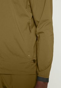 Olive green lightweight jacket with a zipper pocket, drawstring waist, and elastic cuffs. Smooth texture, minimal seam detailing.