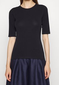 Svart kortärmad topp i mjukt material. Tätsittande design med rund halsringning, slät textur och subtil stretch för komfort.