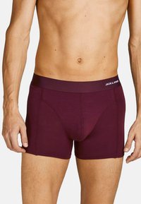 Männershorts in Kastanienrot mit einem elastischen Bund, der den Text "JACK & JONES" trägt. Das Material wirkt weich und hat eine figurbetonte Passform.