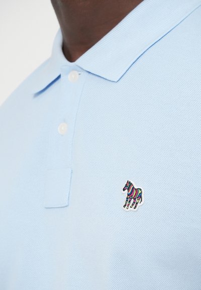 Ανοιχτό μπλε πόλο μπλουζάκι από υφασμάτινη υφή, με πολύχρωμη κεντητή απεικόνιση αλόγου στο αριστερό στήθος, και τρία λευκά κουμπιά στη λωρίδα κλεισίματος.