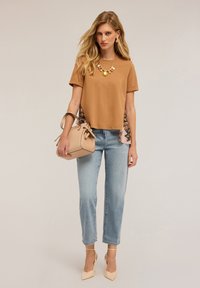 Hnědý tričko s krátkým rukávem a květinovými detaily, světle modré džíny rovného střihu, béžová kabelka a tělové lodičky na vysokém podpatku.