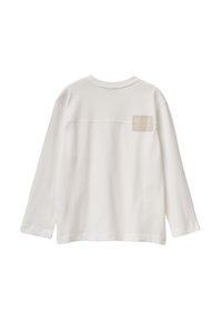 Bílá dlouhá košile s dlouhými rukávy vyrobená z měkké bavlny, s béžovým čtvercovým štítkem na horní části zad s natištěným textem. Jsou viditelné detaily švů.