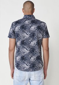Camisa de manga corta en azul marino con un patrón de palmeras; la tela es ligera con una textura suave, con un cuello de solapa.