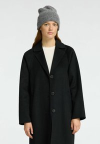 Crni vuneni kaput s reverokragnim ovratnikom i dva prednja gumba, nosi se preko bijele bluze. Uparen je s sivim pletenim beanie šeširom s preklopom.