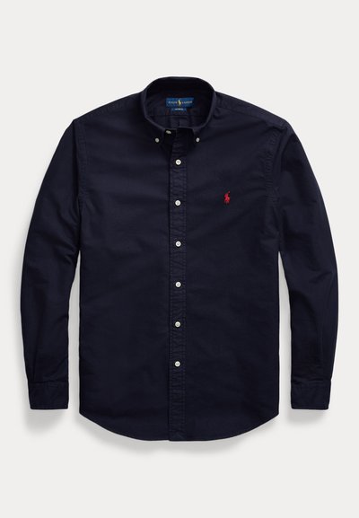 Camicia da uomo blu navy a maniche lunghe con bottoni bianchi e piccolo logo rosso ricamato sul petto.