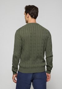 Olivgrön kabelstickad tröja med ribbade muddar och nederkant, som har ett texturerat mönster, medelvikts tyg och en klassisk crew neck-design.