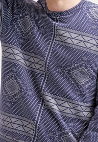 Camicia a maniche lunghe blu navy con un motivo geometrico di diamanti e linee in grigio chiaro. Tessuto morbido con una finitura leggermente strutturata.