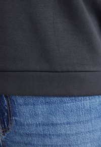 Mørkegrå sweatshirtstoff med ribbet kant kombinert med blå denim, som viser en teksturert overflate og kontrasterende farger.