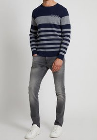 Námořnický a šedý pruhovaný svetr vyrobený z bavlny, s kulatým výstřihem a vyšívaným logem. Spárován se slim-fit šedými džíny a bílými teniskami.