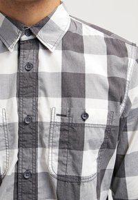 Camicia a maniche lunghe in grigio e bianco a quadri, con colletto classico, due tasche sul petto e bottoni scuri.