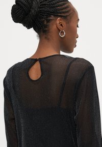 Μαύρο διάφανο τοπ με άνοιγμα στην πλάτη σε σχήμα κλειδιού, υφή με δ�ιακριτική λάμψη και στρογγυλή λαιμόκοψη.