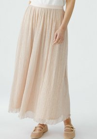 Lichtroze geplooide rok gemaakt van doorschijnende, gestructureerde stof met een elastische tailleband. G gedragen met beige, mesh-achtige schoenen.