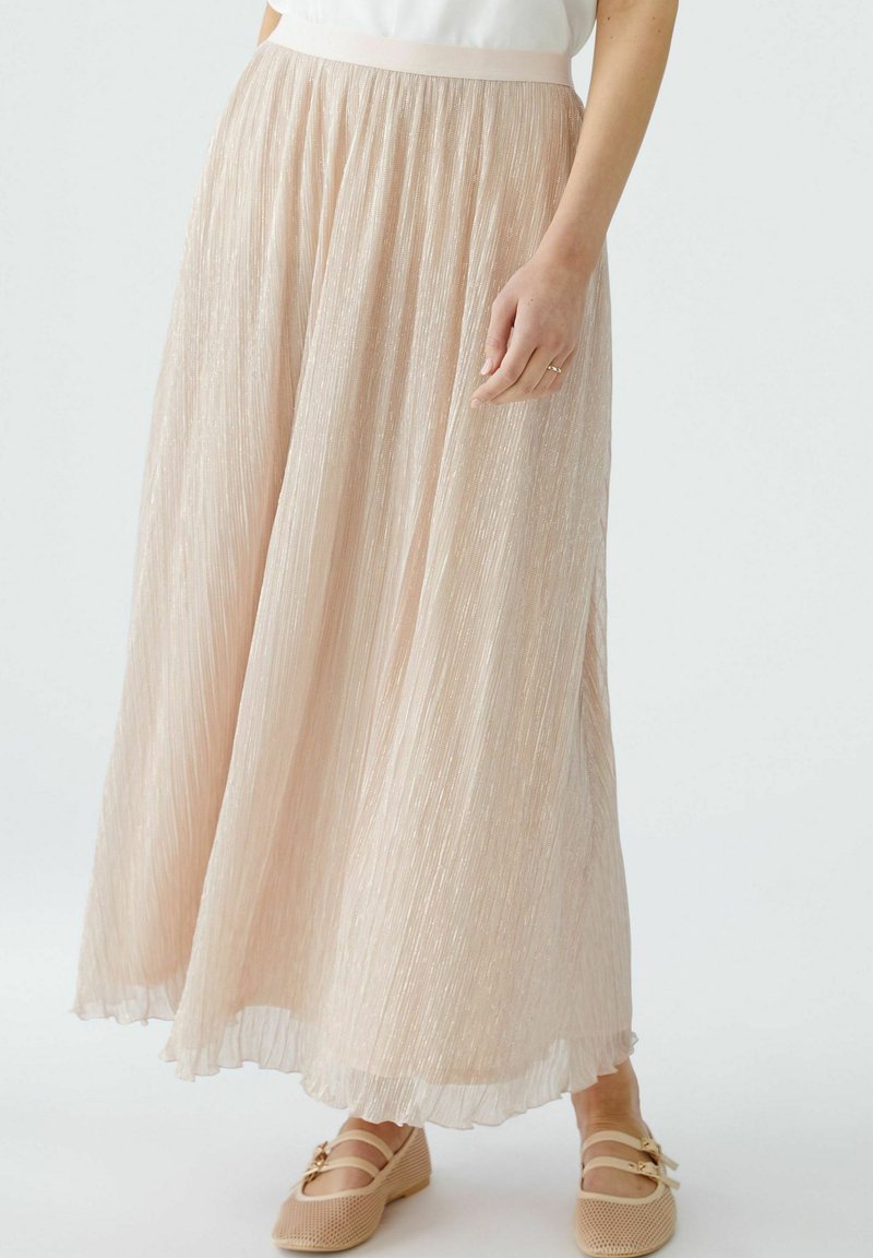Lichtroze geplooide rok gemaakt van doorschijnende, gestructureerde stof met een elastische tailleband. G gedragen met beige, mesh-achtige schoenen.