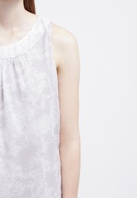 Blusa senza maniche grigia chiara con un motivo texturizzato sottile, scollatura rotonda e vestibilità ampia. Il tessuto sembra morbido e fluido.