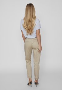 Pantaloni beige a sigaretta in cotone, con orli a risvolto, tasche laterali e design semplice. Indossati con un top azzurro chiaro e tacchi neri.