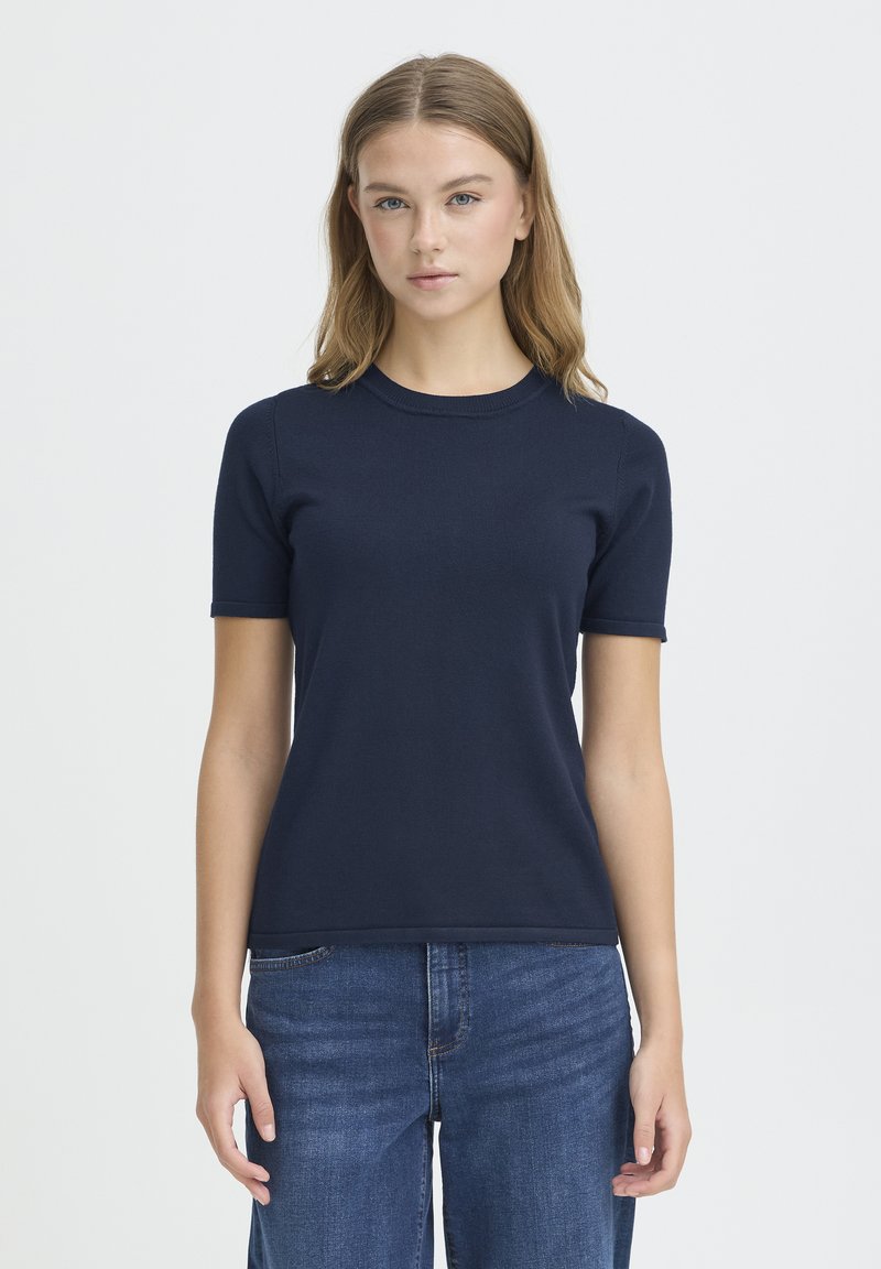 T-shirt bleu marine à manches courtes en tissu lisse. Présente un col rond et une coupe ajustée. Associé à un jean en denim bleu.