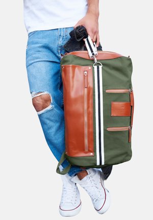 Green and brown duffel bag with a shiny leather finish, multiple zippered pockets, vertical white stripes, and adjustable shoulder strap.