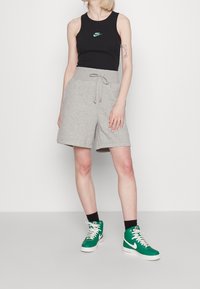 Black sleeveless top with a green Nike logo, paired with gray shorts featuring a drawstring. Green high-top sneakers complete the outfit.