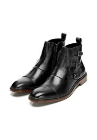 Botas de cuero negro hasta el tobillo con puntera puntiaguda, que cuentan con una cremallera lateral, tres hebillas ajustables y un tacón de madera marrón.