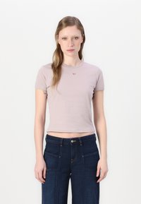 T-shirt viola chiaro a maniche corte con scollatura rotonda e piccolo dettaglio del logo rosso sul petto, abbinato a jeans a gamba larga blu scuro.