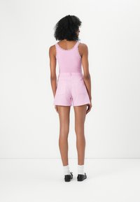 Rosa ribbet tanktop med blonderkant kombinert med rosa stripete shorts. Modell med hvite sokker og svarte sko, sett fra bak.
