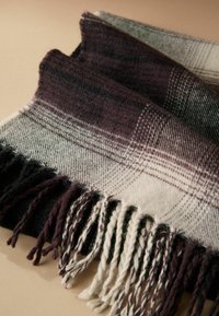 Plaid wool scarf featuring burgundy, gray, and black hues. Edges lined with twisted fringe for added texture. Soft and warm material.