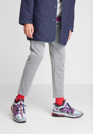 Person wearing gray pinstripe pants, red socks, white and purple sneakers, and a navy blue coat, standing on a light gray floor.