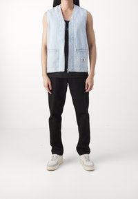 Světle modrá džínová vesta bez rukávů, zapínání na zip vpředu, dvě přední kapsy, logo na levé kapse, kombinována s černými kalhotami a teniskami.