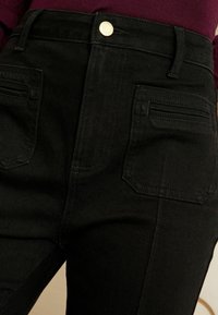 Černé džíny s vysokým pasem a zlatým knoflíkem, vybavené dvěma předními a dvěma zadními kapsami, prezentující čistý a elegantní design.