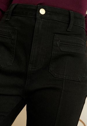 Black denim high-waisted pants with gold button, featuring two front pockets and two back pockets, showcasing a clean, sleek design.