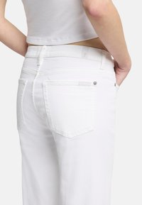 Weiße Denim-Jeans mit geradem Schnitt, ausgestattet mit zwei Gesäßtaschen, minimalistischem Design und einem dezenten Markenlabel oberhalb der rechten Tasche.