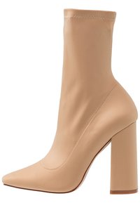 Bottine beige en tissu lisse avec bout pointu, talon bloc haut et coutures décoratives le long de la couture supérieure.