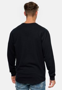 Schwarzes Langarmshirt aus strukturiertem Stoff, mit Rundhalsausschnitt und gerippten Bündchen. Kombiniert mit blauen, ausgewaschenen Jeans.