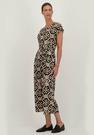 Zwarte jumpsuit met een bloemenpatroon in beige, korte mouwen, cinchter taille en cropped pijpen. Gekocht met zwarte instappers.