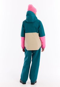 Barevná zimní bunda s panely v teal, růžové a béžové barvě, vybavená kapucí, elastickými manžetami a odpovídajícími kalhotami. Texturovaná látka s aerodynamickým designem.