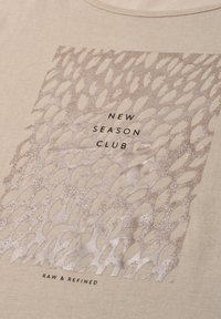 Beige fabric with textured abstract pattern and the text "NEW SEASON CLUB" and "RAW & REFINED" printed on it.