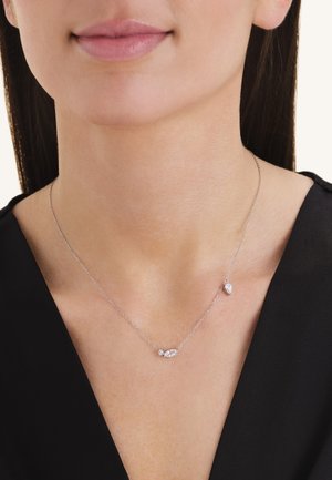 Delicate silver necklace with three small clear gemstones worn on a woman in a black top, showing neck and lower face.