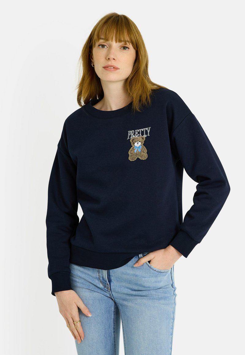Sudadera azul marino con puños y dobladillo acanalados. Presenta el texto "PRETTY" y un diseño bordado de un oso de peluche en el pecho.