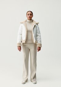 Kurtka puchowa w białym kolorze z beżowym kołnierzem i mankietami z futra syntetycznego. Dopasowany krój z gładką zewnętrzną fakturą. Połączona z beżowymi spodniami i sneakersami.